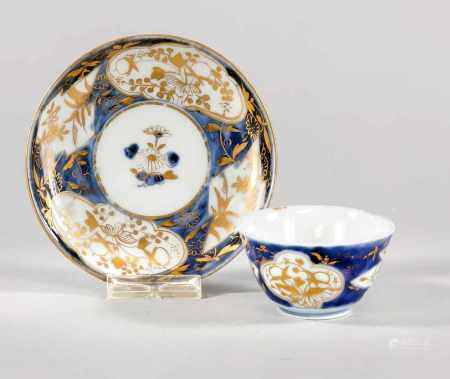 Tasse & Untertasse, China, 18. Jh., Dekor in Unterglasur-Blau (Kobaltblau) und Gold in Aufglasur. Untertasse im Spiegel mit Blume, von einer breiten Bordüre mit passig geschweiften Kartuschen in alternierender Form gerahmt. Dieser Dekor wird auf der Au?enwandung der Tasse fortgeführt. Dekor stellenweise ber., H. ca. 4 cm/D. Teller 11 cm