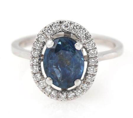 A sapphire and diamond ring set with an oval-cut sapphire weighing app. 2.18 ct. encircled by numerous brilliant-cut diamonds weighing a total of app. 0.25 ct., mounted in 18k white gold. Front app. 12.0×14.5 mm. Size 55.